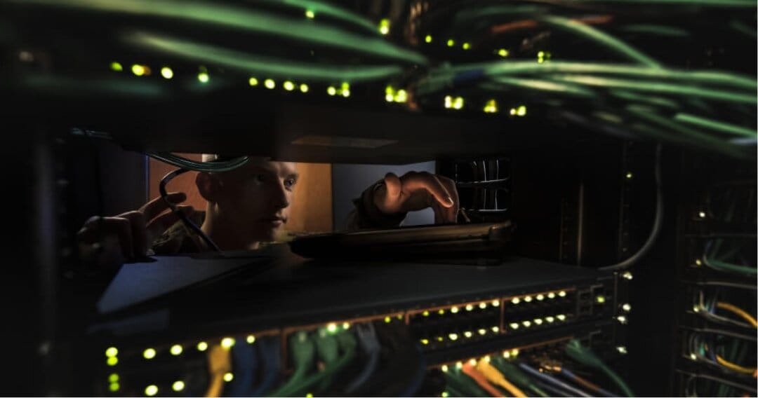 An Air Force engineer looks at a an electric panel with several cords and lights.